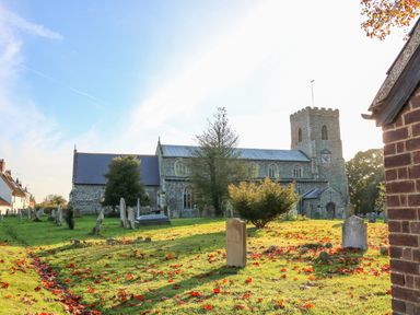 An old stone church with a bell tower and gravestones on a grassy area with scattered leaves at 27 Whitegates in Ludham