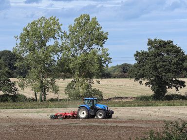 A blue tractor plowing a field with trees in the background at 27 Whitegates in Ludham
