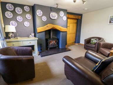 A sitting room with a wood burning stove three brown leather armchairs a white side table and decorative plates on a dark blue wall at Pen Y Bryn Cottage in Llandudno