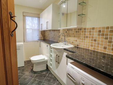 A utility room with a washing machine a sink a toilet and cabinets at Pen Y Bryn Cottage in Llandudno