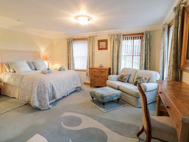 A bedroom with a bed sofa ottoman wooden desk chair and chest of drawers at Pen Y Bryn Cottage in Llandudno