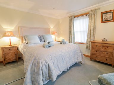 A bedroom with a bed with rolled towels bedside tables with lamps a window with curtains and a wooden dresser at Pen Y Bryn Cottage in Llandudno
