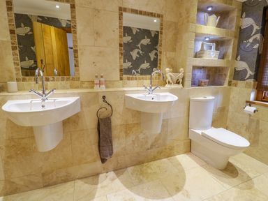 A bathroom with two sinks mirrors a toilet and built in shelves at Pen Y Bryn Cottage in Llandudno