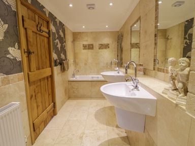 A bathroom with two sinks a bathtub a wooden door and decorative figurines at Pen Y Bryn Cottage in Llandudno