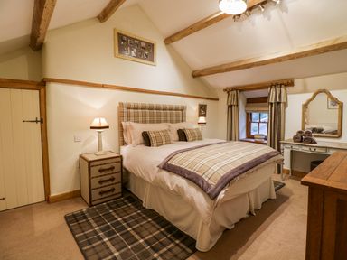 A bedroom with a double bed plaid bedding wooden beams bedside tables lamps and a dressing table at Pen Y Bryn Cottage in Llandudno