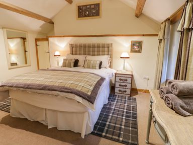 A bedroom with a large bed covered in plaid bedding two bedside tables with lamps a wall mirror folded towels on a wooden table and a window with curtains at Pen Y Bryn Cottage in Llandudno