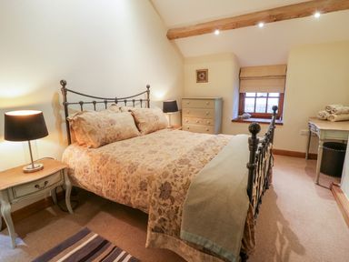 A bedroom with a double bed a bedside table with a lamp a chest of drawers a window and a desk at Pen Y Bryn Cottage in Llandudno