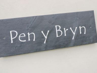 A close up of a dark stone sign with white lettering reading Pen y Bryn on a light wall at Pen Y Bryn Cottage in Llandudno