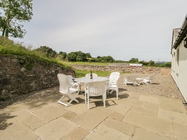 An outdoor patio area with white plastic chairs and table with a bottle on it at Pen Y Bryn Cottage in Llandudno