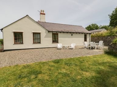 An outdoor area with white chairs and tables beside a single-story house at Pen Y Bryn Cottage in Llandudno