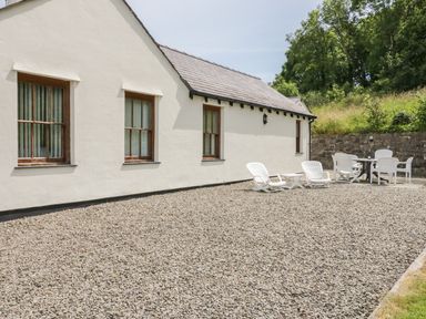 A white cottage with gravel ground and outdoor white chairs around a table at Pen Y Bryn Cottage in Llandudno