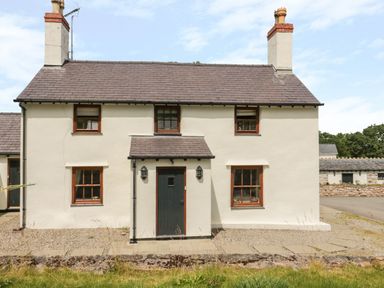 A two story house with white walls and a dark door in a rural setting at Pen Y Bryn Cottage in Llandudno