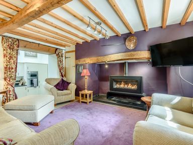 A living room with beige sofas a purple rug a fireplace and a wall-mounted television at Pen Y Bryn Cottage in Llandudno