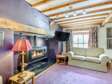 A living room with a fireplace a beige sofa a window with floral curtains and a red lamp at Pen Y Bryn Cottage in Llandudno