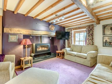 A living room with exposed wooden beams a fireplace a wall-mounted TV beige sofas and floral curtains at Pen Y Bryn Cottage in Llandudno