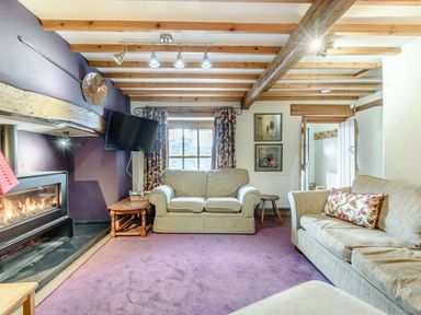 A living room with two beige sofas a wall mounted TV a fireplace and purple carpet at Pen Y Bryn Cottage in Llandudno