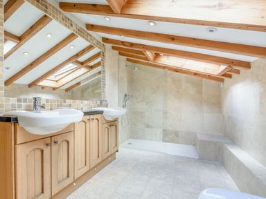 A bathroom with two sinks wooden cabinets a large mirror a shower area and wooden ceiling beams at Pen Y Bryn Cottage in Llandudno