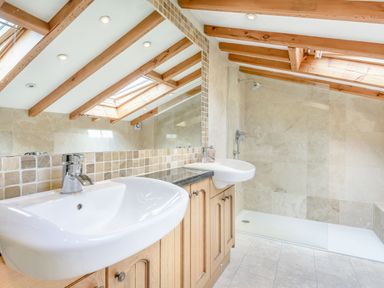 A bathroom with two white sinks on a wooden cabinet under a mirror and a shower area with glass partition under skylights at Pen Y Bryn Cottage in Llandudno