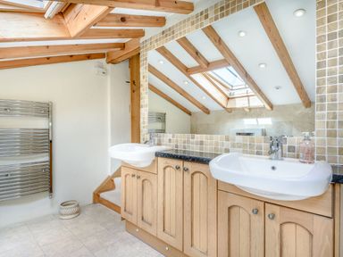 A bathroom with two sinks wooden cabinets a large mirror and exposed wooden beams at Pen Y Bryn Cottage in Llandudno