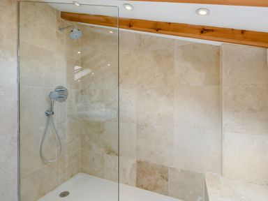 A shower area with beige tiled walls and a glass partition at Pen Y Bryn Cottage in Llandudno