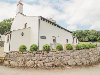 A white house with a stone wall and shrubs outside at Pen Y Bryn Cottage in Llandudno