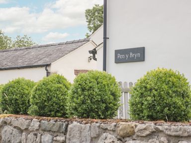 Green bushes along a stone wall outside a white building with a sign that reads Pen y Bryn in Llandudno