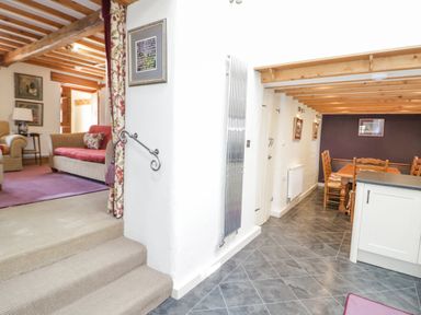 A room with carpeted steps leading to a living area with sofas and a wooden beam ceiling next to a dining area with wooden chairs and a table at Pen Y Bryn Cottage in Llandudno