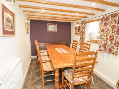 A dining room with a wooden table and chairs with floral cushions and curtains at Pen Y Bryn Cottage in Llandudno