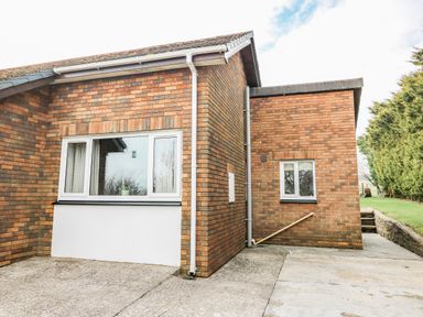 The exterior of a brick building with two windows concrete driveway and a grassy area with trees at Blaenywawr Annexe in Lampeter