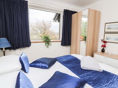 A bedroom with blue pillows and bed runner a wardrobe a bedside table with a vase of flowers and framed pictures at Blaenywawr Annexe in Lampeter