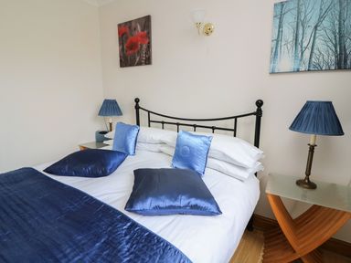 A bedroom with a double bed blue cushions two bedside tables with blue lamps and wall art at Blaenywawr Annexe in Lampeter