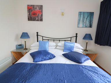A bedroom with a double bed with blue pillows and lamps at Blaenywawr Annexe in Lampeter