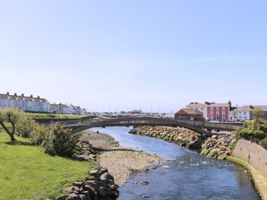 A river with a pedestrian bridge and colorful houses in the background at Blaenywawr in Lampeter