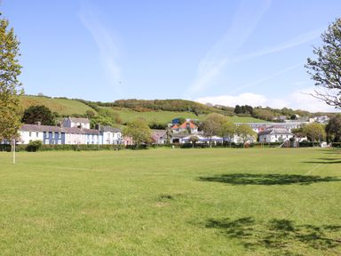 A large grassy field with houses and trees in the background under a clear sky at Blaenywawr in Lampeter