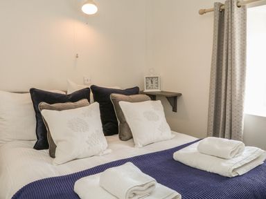 A bed with multiple pillows and folded towels on a blanket near a window with curtains at Wren Cottage in Ilfracombe
