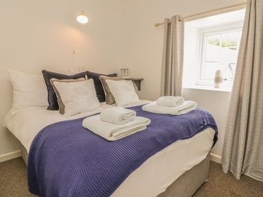 A bedroom with a bed with pillows and towels near a window with curtains at Wren Cottage Ilfracombe