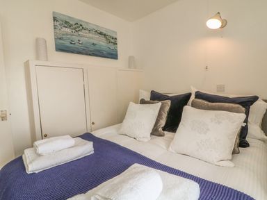 A bedroom with a bed with multiple pillows and folded towels on a purple blanket at Wren Cottage in Ilfracombe
