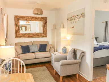 A living room with a sofa with cushions an armchair a lamp and a mirror on the wall at Wren Cottage in Ilfracombe