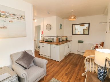 A small living area with an armchair a kitchen counter with a microwave and appliances and a wooden dining table with chairs at Wren Cottage in Ilfracombe