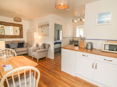 A kitchen and living area with a dining table, sofa, armchair, and kitchen appliances at Wren Cottage in Ilfracombe