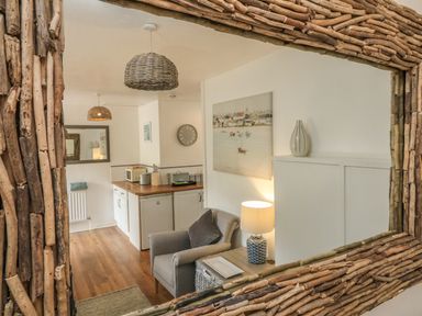 A small kitchen and sitting area with a chair, lamp, and wooden countertops reflected in a rustic framed mirror at Wren Cottage in Ilfracombe