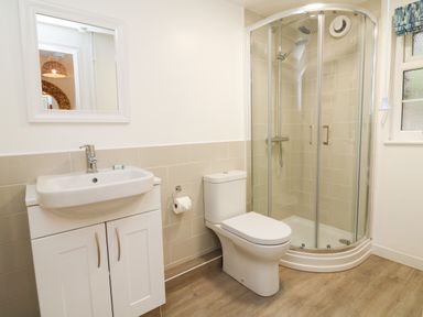 A bathroom with a sink cabinet a toilet and a corner shower with glass doors at Martin Cottage in Ilfracombe