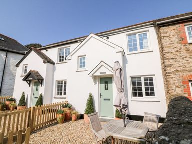 A white two-story cottage with green doors and potted plants outside a wooden fence at Martin Cottage in Ilfracombe