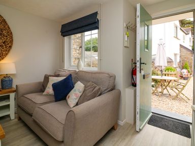 A living room with a sofa near a window and an open door leading to an outdoor seating area at Martin Cottage in Ilfracombe