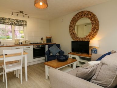 A kitchen and living area with white cabinets wooden furniture and a large round mirror at Martin Cottage in Ilfracombe