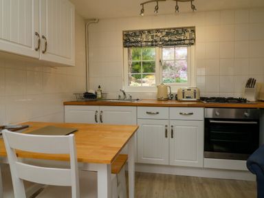 A kitchen with white cabinets wooden countertop and a table with a chair at Martin Cottage in Ilfracombe