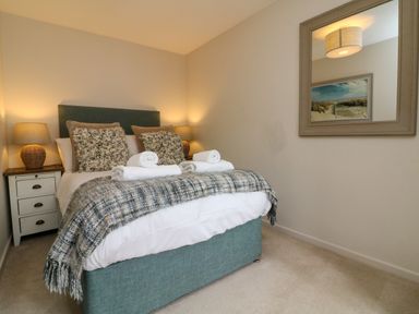 A bedroom with a bed with pillows and rolled towels bedside tables with lamps and a wall mirror at Martin Cottage in Ilfracombe