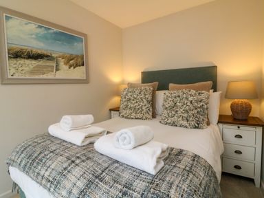 A bedroom with a bed pillows bedside tables lamps and a beach painting at Martin Cottage Ilfracombe