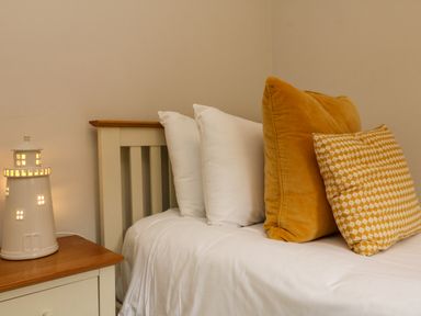 A bed with white and yellow pillows next to a nightstand with a lighthouse-shaped lamp at Martin Cottage in Ilfracombe
