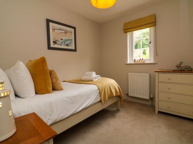 A single bed with white and mustard pillows and folded towels beside a window with a yellow blind and a chest of drawers with a decorative rabbit at Martin Cottage Ilfracombe